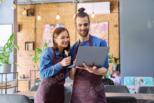 Preview: Young man and woman workers owners in aprons using laptop, inside restaurant cafe