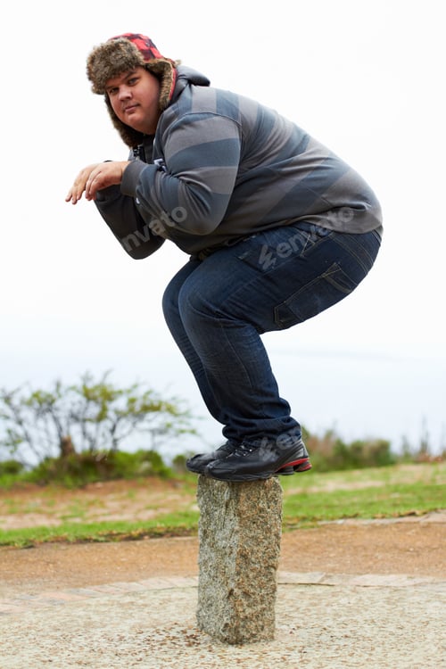 Preview: Ready to pounce. An overweight young man in winter wear balancing playfully on a post.