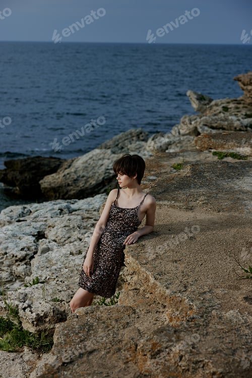 Preview: woman in a shiny dress stands on the stone coast of the ocean nature unaltered