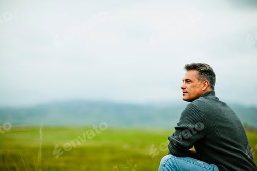 Preview: A man sitting alone looking into the distance, deep in thought.