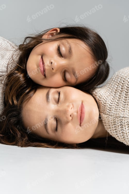 Preview: mother and daughter in warm sweaters lying with closed eyes on grey background
