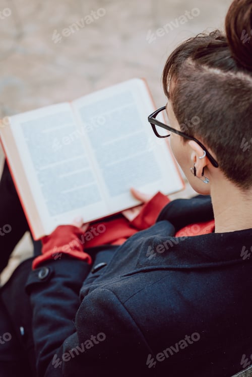 Preview: Young woman reading book on bench in park