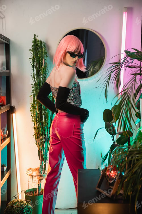 Preview: Fashionable drag queen in sunglasses and gloves looking at camera near plants at home
