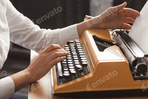 Preview: Closeup female writer hands typing on a yellow vintage mechanical typewriter