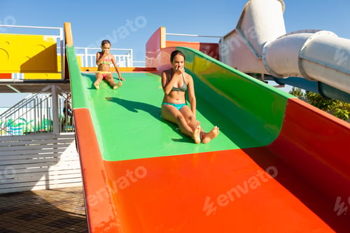 Preview: Two lovely sisters descend from a multi-colored bright slide into a pool with clear transparent