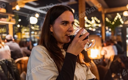 Preview: Young woman drinking dark beer on a night out in pub
