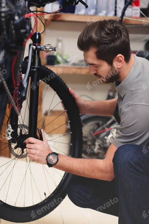 Preview: young male worker in apron fixing bicycle in workshop
