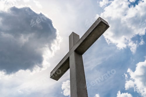 Preview: A large concrete cross on a cemetery against a blue sky with white clouds.