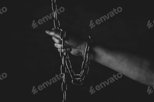 Preview: Person with their fingers gripping a metal chain in a dark setting