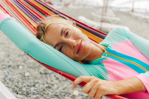 Preview: Happy smiling carefree young woman relaxing in a hammock on the beach.