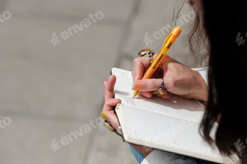 Preview: Close-up of female hands writing on a notebook outdoors.