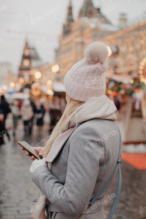 Preview: Young woman with phone at the street in Christmas holiday