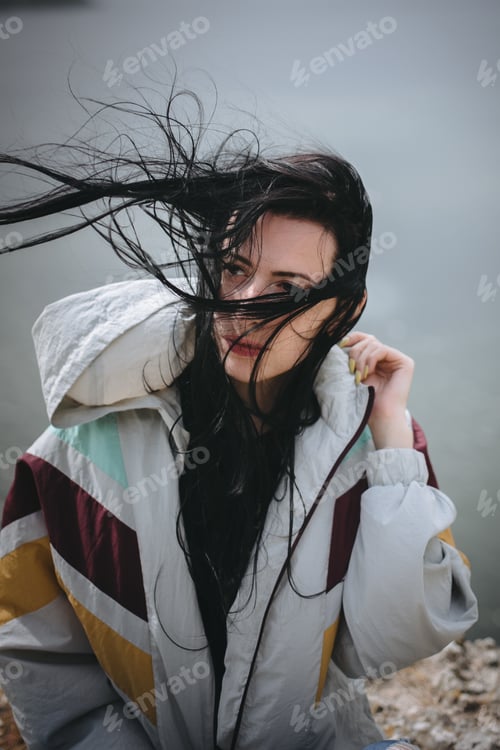 Preview: Stylish hipster girl with windy hair sitting on top of rock mountain with beautiful view on river