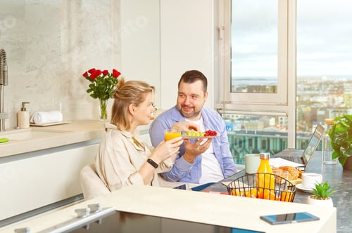 Preview: Young beautiful happy couple having breakfast together in kitchen at home. Lifestyle