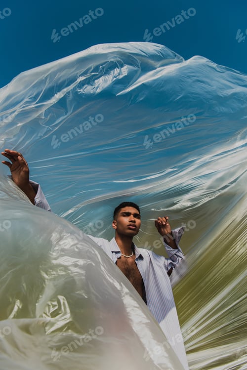 Preview: stylish african american man near cellophane film under blue sky