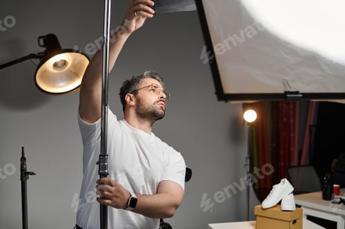 Preview: Creative professional adjusting lighting during a product shoot in a modern studio
