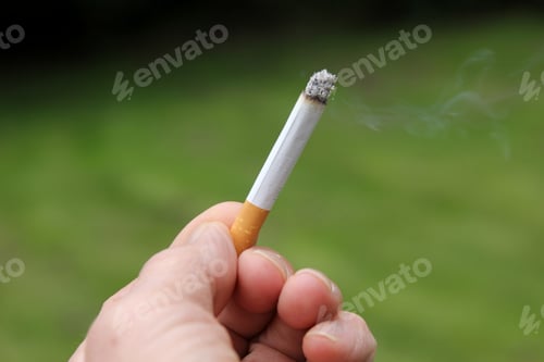 Vorschau: Nahaufnahme der Finger eines Mannes, der eine Zigarette hält, mit verschwommenem grünem Hintergrund