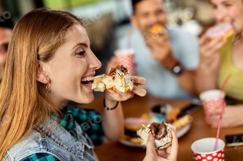 Preview: Happy woman and her friends eating glazed donuts in a cafe.