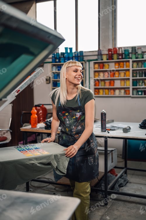 Preview: Female print shop worker silkscreen printing at workshop.