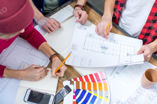 Preview: Close-up partial view of male and female designers working at project with blueprints