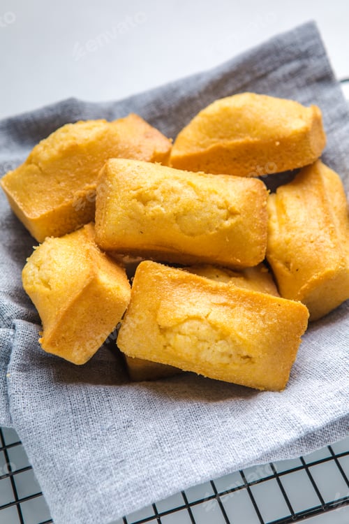 Preview: Close-up of corn muffins on plate with bowl of corn meal and additional muffins in the background.