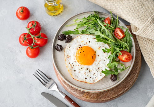 Preview: Fried eggs with arugula, ovives and cherry tomatoes on a plate on a wooden board
