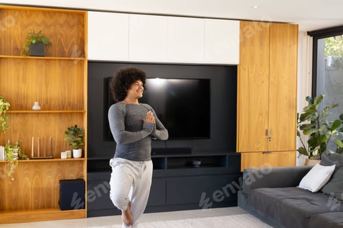Preview: Man balancing in yoga pose in living room in sportswear near flat-screen TV with built-in shelving