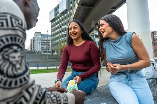 Preview: Diverse young friends playing cards and laughing outdoors