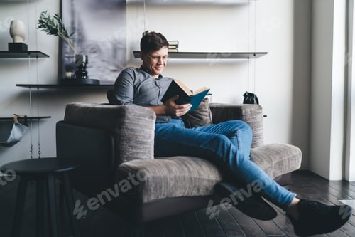 Preview: Smiling young man reading book in living room