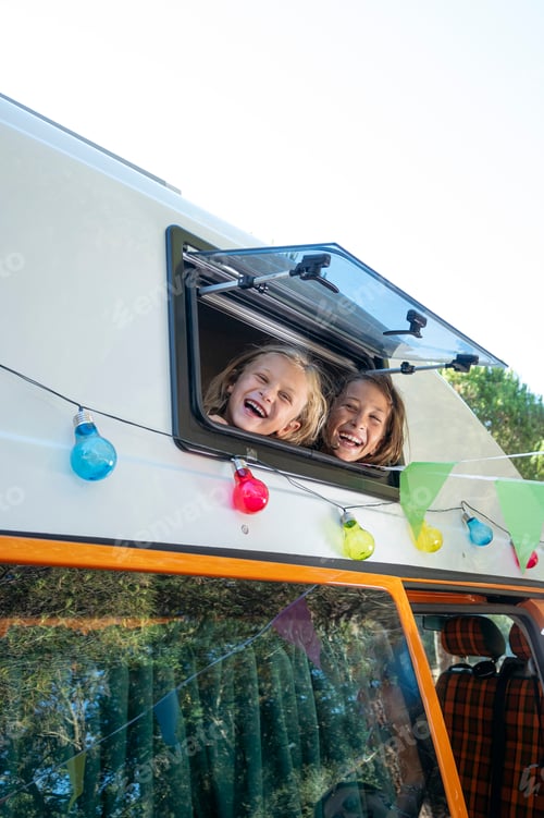 Preview: Happy children stick their heads out of the van window on a wonderful day of camping.