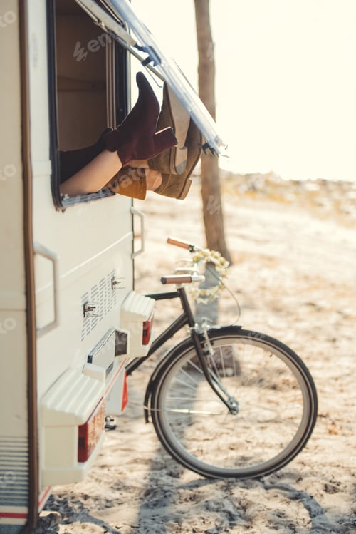 Preview: couple resting in trailer with feet outside, bicycle near campervan