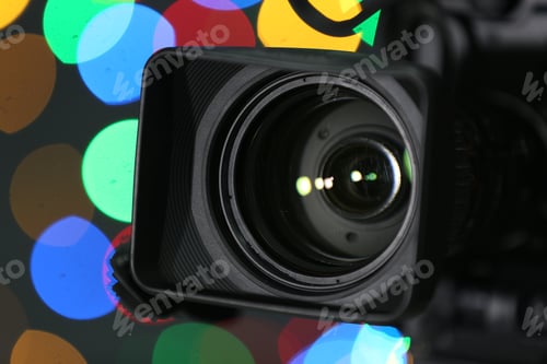 Preview: Modern video camera against blurred colorful lights, closeup