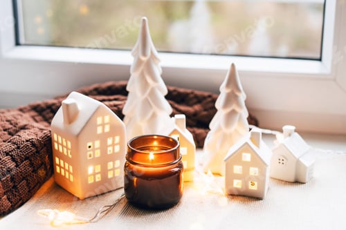 Visualização: Cena de Natal aconchegante com casas de cerâmica e luz de velas perto de uma janela