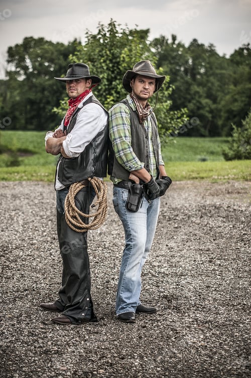 Preview: Vertical shot of tow males wearing a cowboy outfit while standing back to back