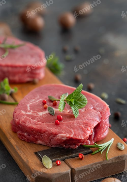 Preview: Raw beef fillet steaks with herbs and spices on wooden board on dark background close up
