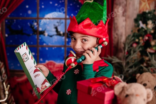 Preview: Young child dressed as an elf talks on a toy phone beside Christmas gifts and a festive background