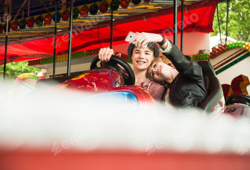 Preview: Teenage couple sitting in bumper car photographing themself with smartphone