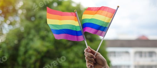 Preview: hands showing LGBTQ Rainbow flag on green nature background. Pride month concept