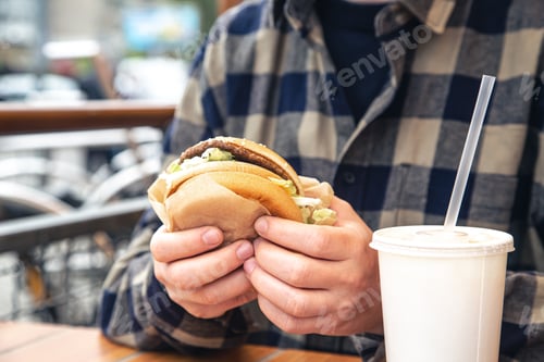Preview: Burger in male hands close-up in a fast food cafe.