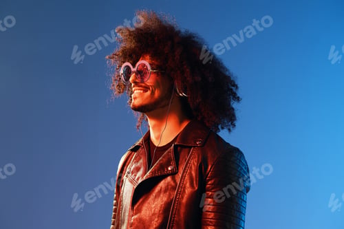 Preview: Portrait of a stylish man with curly hair with glasses and headphones on a blue background