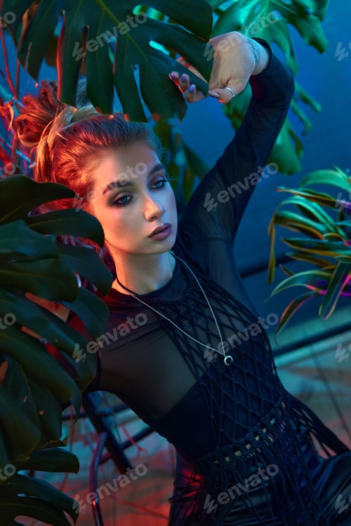 Preview: Young woman surrounded by vibrant tropical plants, wearing black leather outfit and long-sleeved