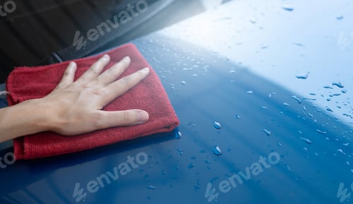 Preview: Car wash service. Man hand holding red microfiber cloth polish blue car and water drop after clean