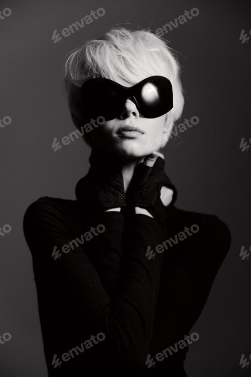 Preview: Elegant woman in black attire posing confidently, wearing large sunglasses and stylish gloves