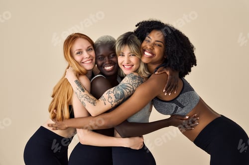 Preview: Happy fit sporty diverse girls wearing sportswear hugging at beige background.