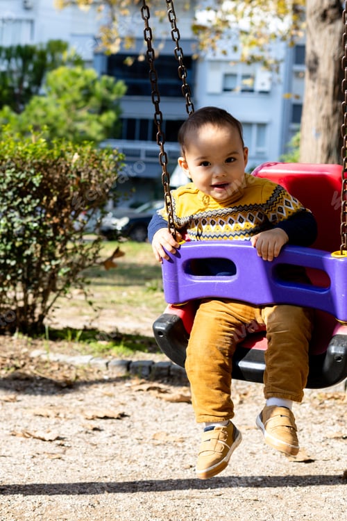 Preview: Cute baby boy having fun on outdoor playground. Toddler activities. Happy baby swinging on swing.