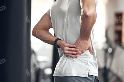 Preview: Closeup of one mixed race man holding his sore lower back while exercising in a gym. Guy suffering