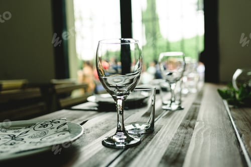 Preview: Wooden tables with cutlery plates and backlit glasses without anyone.