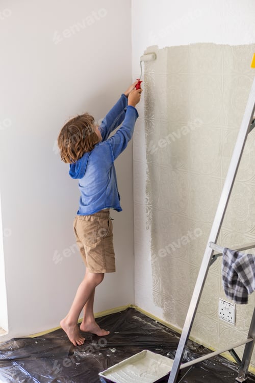 Preview: Eight year old boy using paint roller to paint a house wall