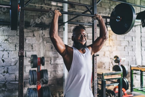 Preview: Muscular black sportsman lifting heavy barbell in gym