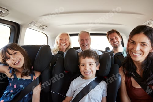 Preview: Three generation white family sitting in two rows of passenger seats in a car, smiling to camera